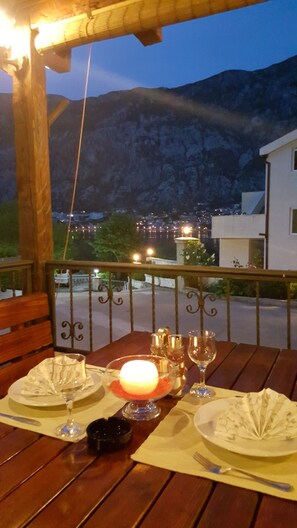 A wooden table set for two with a candle, glasses, and a small bowl on a balcony overlooking a mountainous landscape. - Hotel Galia (Kotor)
