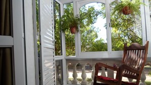 A rocking chair in a sunlit room with large windows, a potted plant, and a view of trees outside. - La Casona de Susana (Colon)