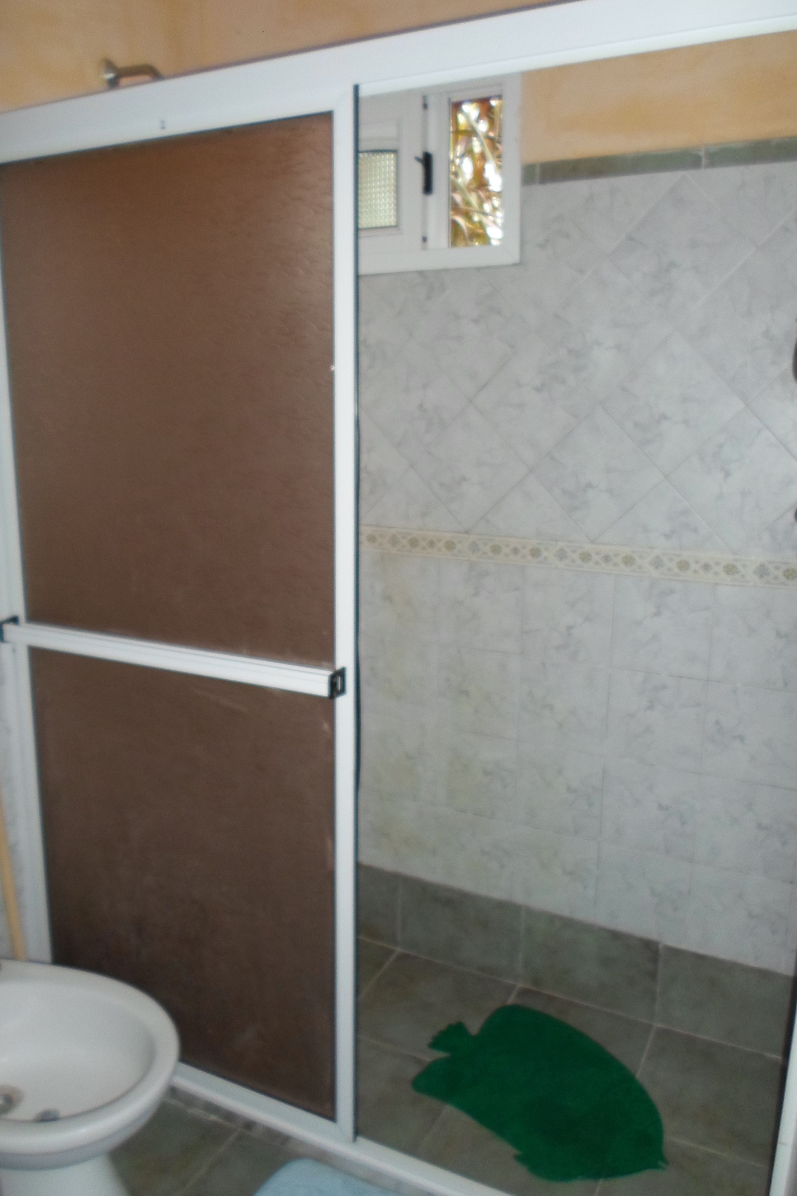Un baño con inodoro, ducha con tapete verde y pared de azulejos con un borde decorativo.