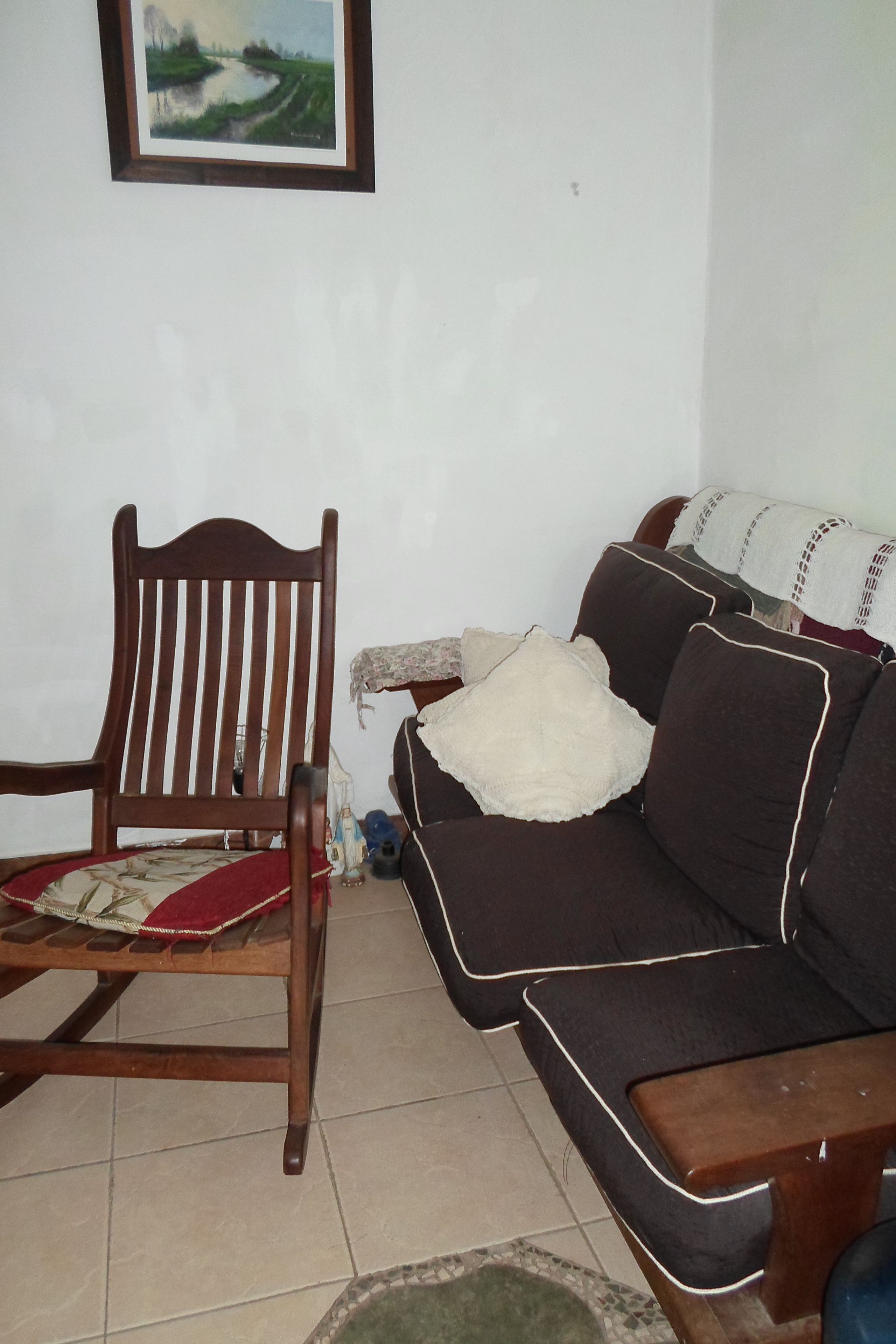 Un salon avec une chaise en bois, un canapé foncé agrémenté d’un coussin blanc et un tableau encadré accroché au mur.