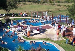 En stor udendørs swimmingpool med flere afdelinger, omgivet af liggestole og parasoller.