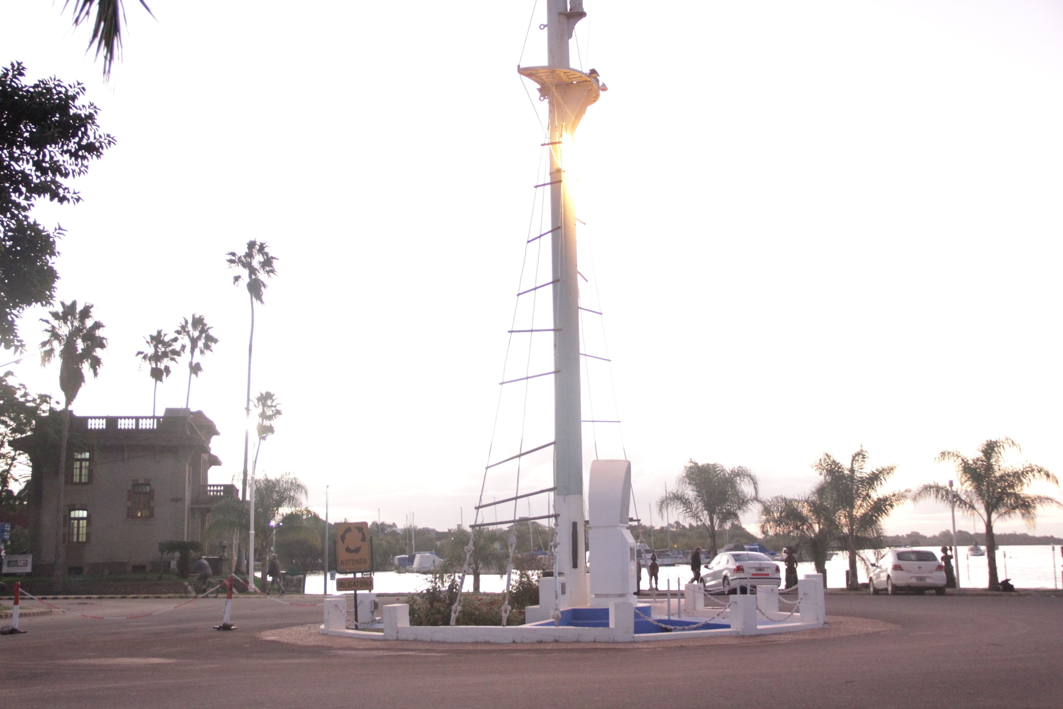 A tall, white monument with a sail-like structure, surrounded by palm trees and a body of water.