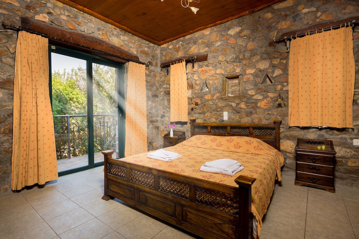A bedroom with a stone wall, a wooden bed, and a view through a glass door.