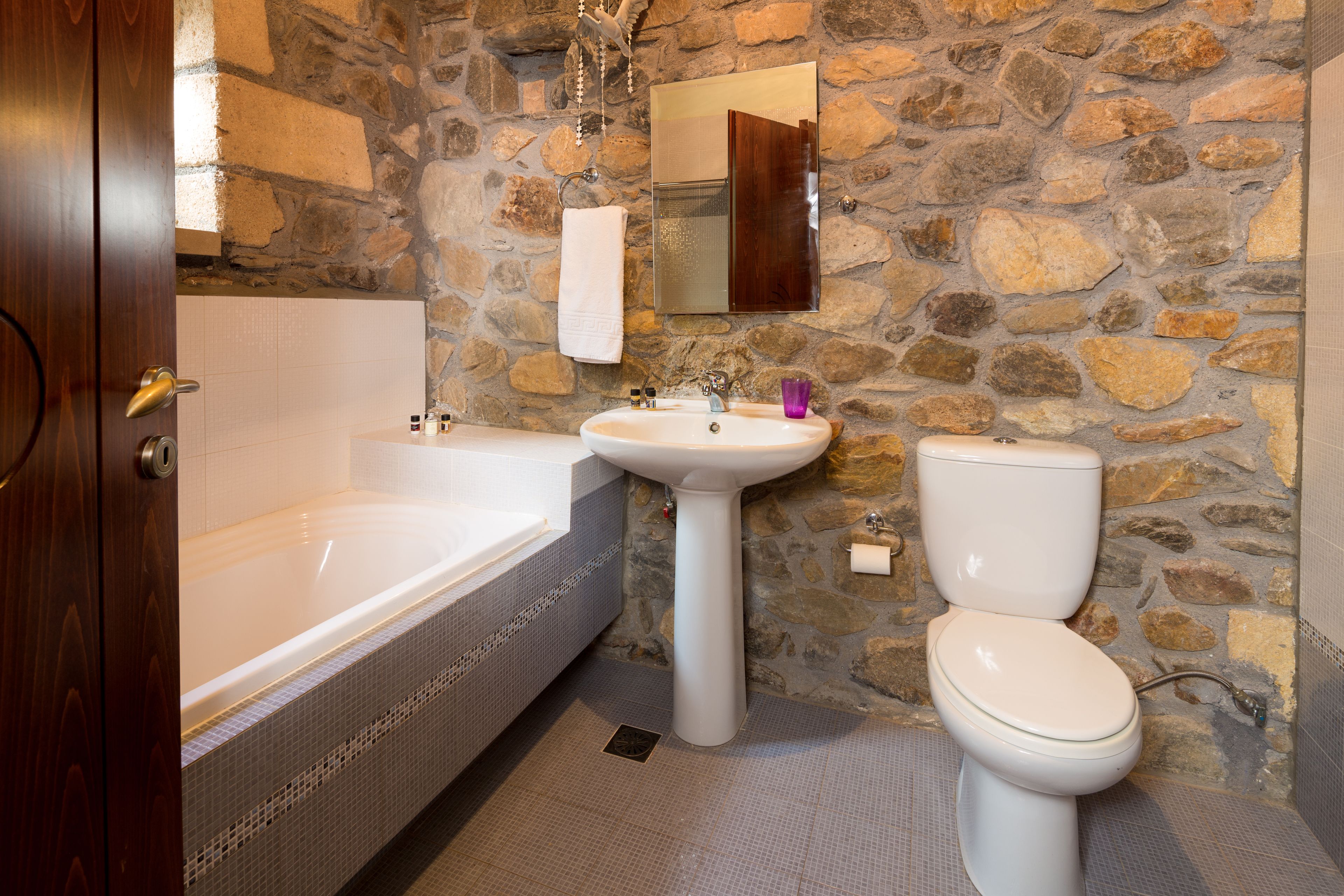 A bathroom with a stone wall, a bathtub, a sink, and a toilet.