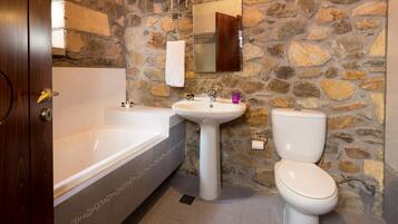 A bathroom with a stone wall, a bathtub, a sink, and a toilet.