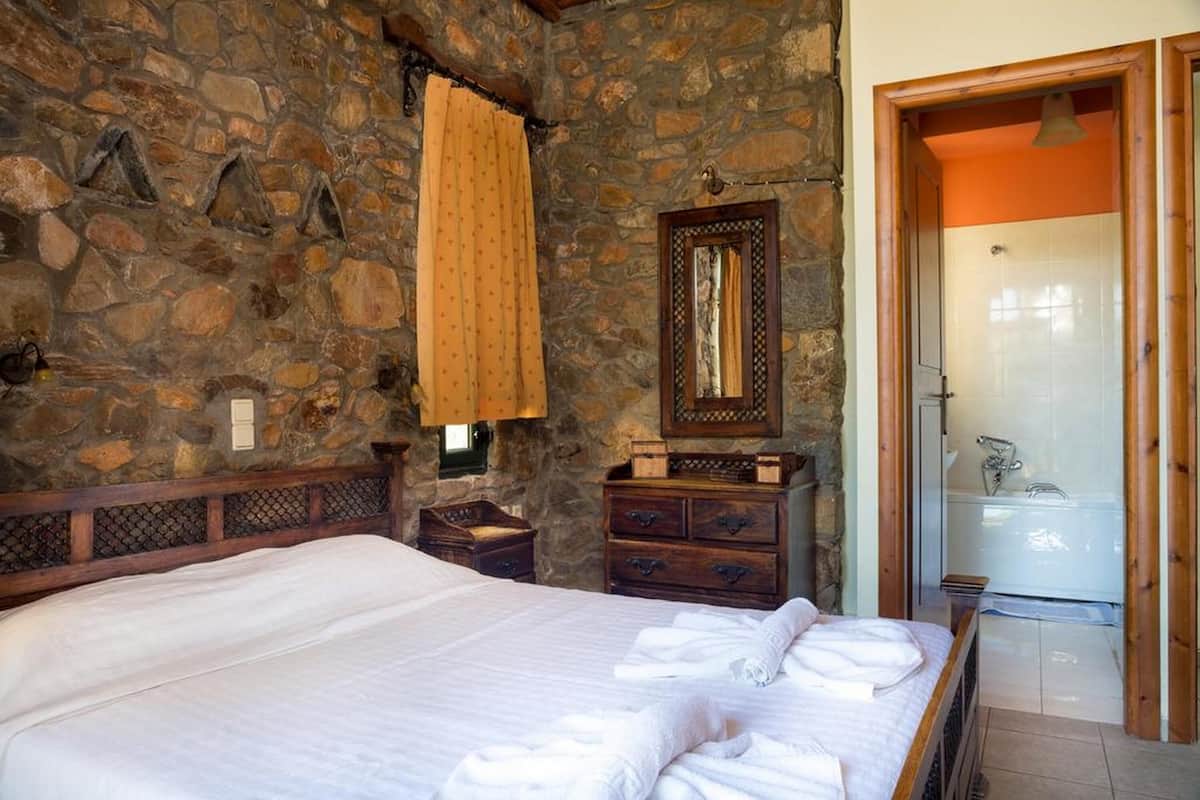 A bedroom with a stone wall, a wooden bed, a dresser, and a bathroom with a glass shower.