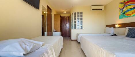 A hotel room with two beds, a TV mounted on the wall, an air conditioning unit, and a colorful abstract painting.