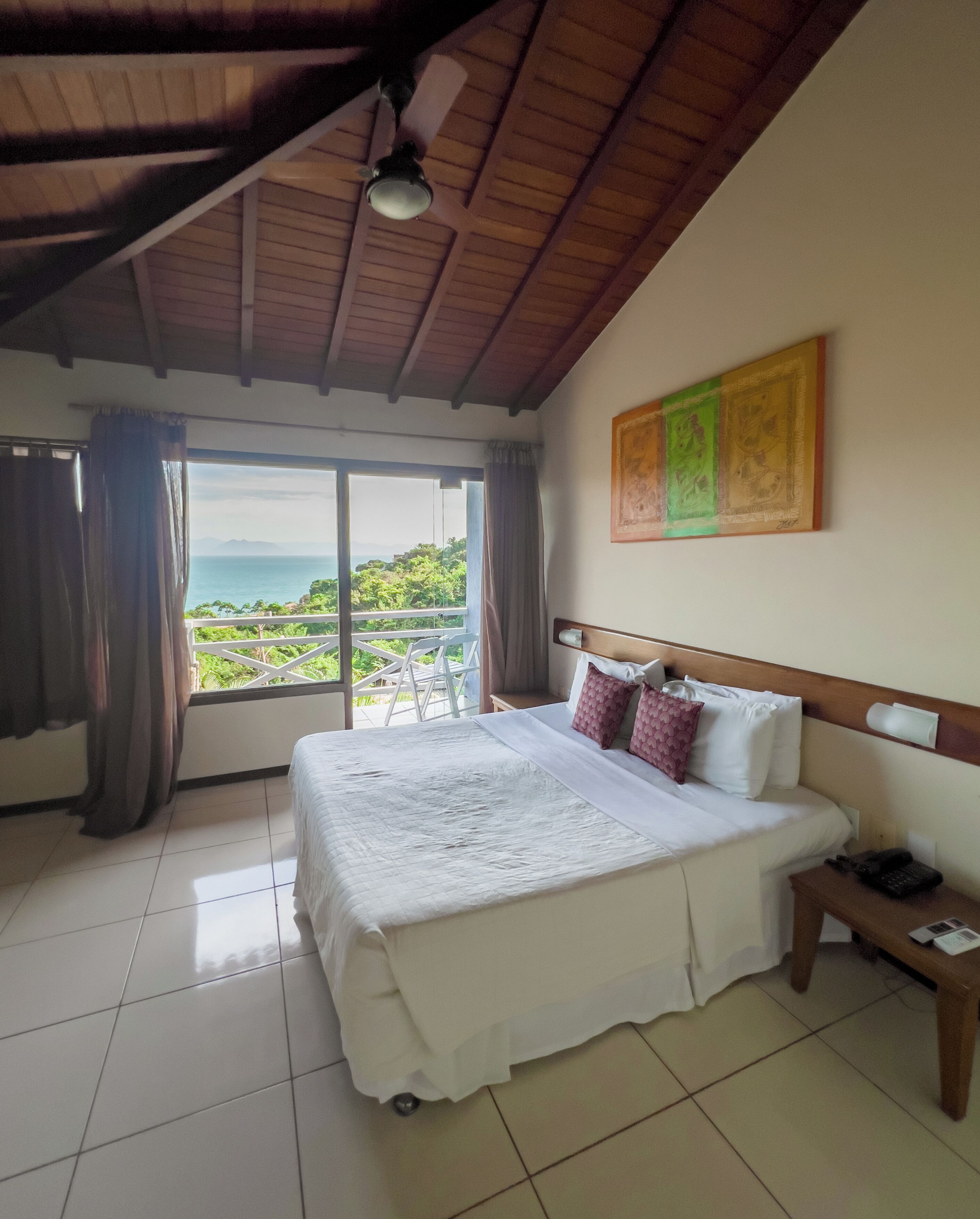 Una habitación de hotel con una cama, una mesita de noche, un cuadro y vista al océano.