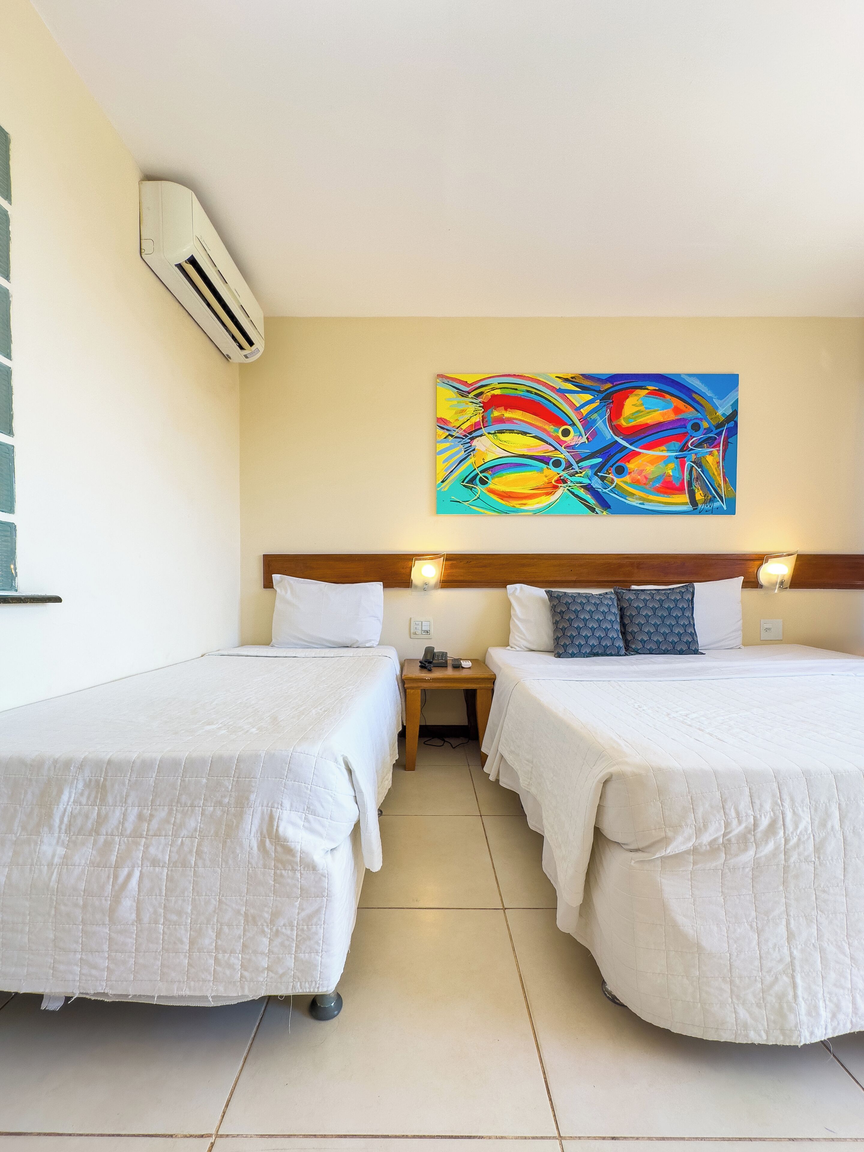 Habitación de hotel con dos camas, un cuadro en la pared y un equipo de aire acondicionado.