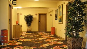 A hallway with a patterned carpet, a potted plant, and a trash can.