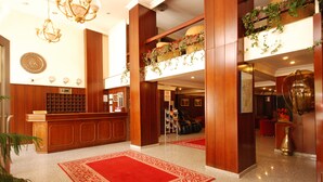 A hotel lobby with a reception desk, red carpet, and wooden decor.