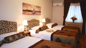 A hotel room with two beds, patterned headboards, bedside lamps, a painting on the wall, and a window with curtains.