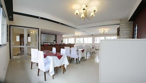 A spacious dining area with round tables covered in white tablecloths and chairs, a bar area with a counter and bar stools, and a stone accent wall. - Hotel Cá Doro (Mar del Plata)