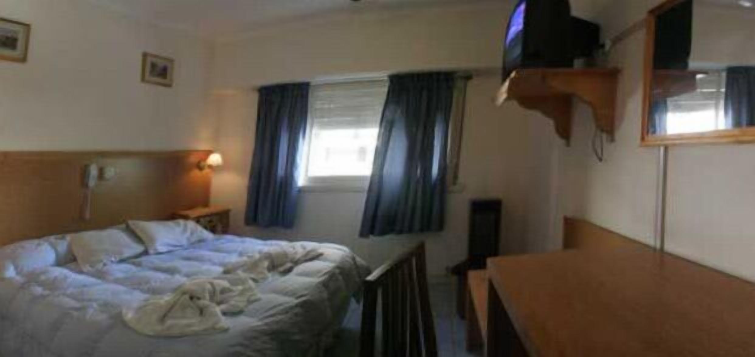 A hotel room with a bed, a desk, a television, and a window with curtains.