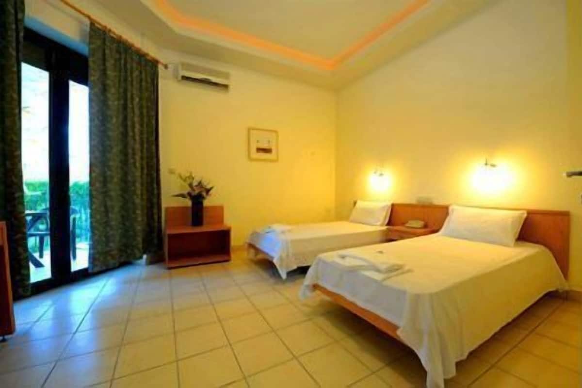 Ein Hotelzimmer mit zwei Betten, einem kleinen Tisch mit einer Pflanze, einem Fenster mit Vorhängen und einer Wand-Klimaanlage.