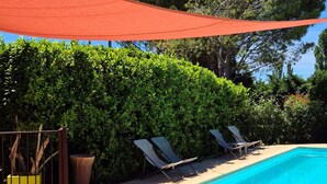 Una piscina con sillones de descanso y un seto grande.