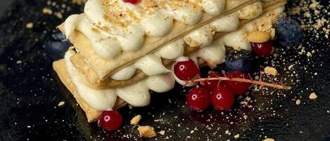 A dessert on a dark plate with white cream, berries, and crumbs.