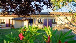 Un edificio con techo de tejas, un patio cercado y un pequeño jardín con flores rosadas.