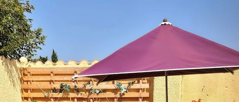 A patio area with outdoor furniture, a wooden planter wall, and a purple umbrella.