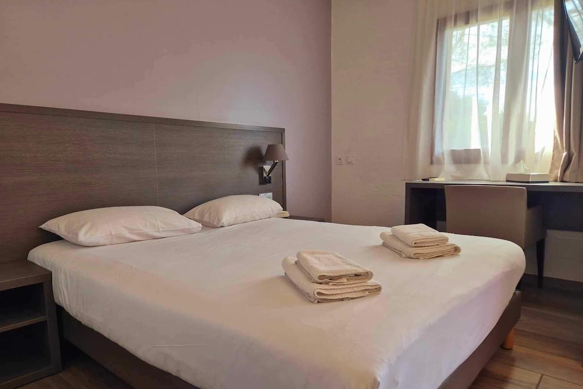 A neatly made bed with white linens and two folded towels on the bed.