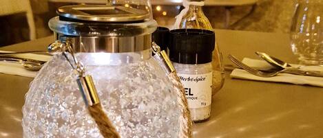 A table with a crystal glass pitcher, a bottle of herb oil, and a metal container.