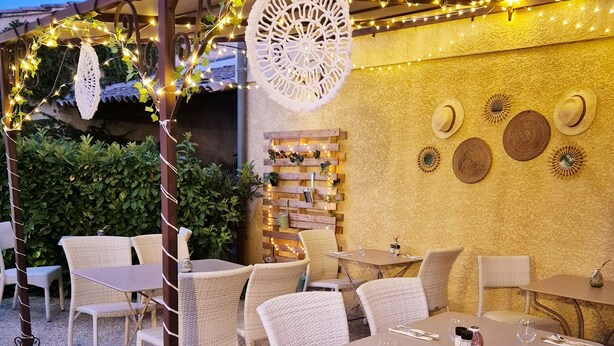 Un patio al aire libre con mobiliario de mimbre, luces colgantes y adornos en las paredes.