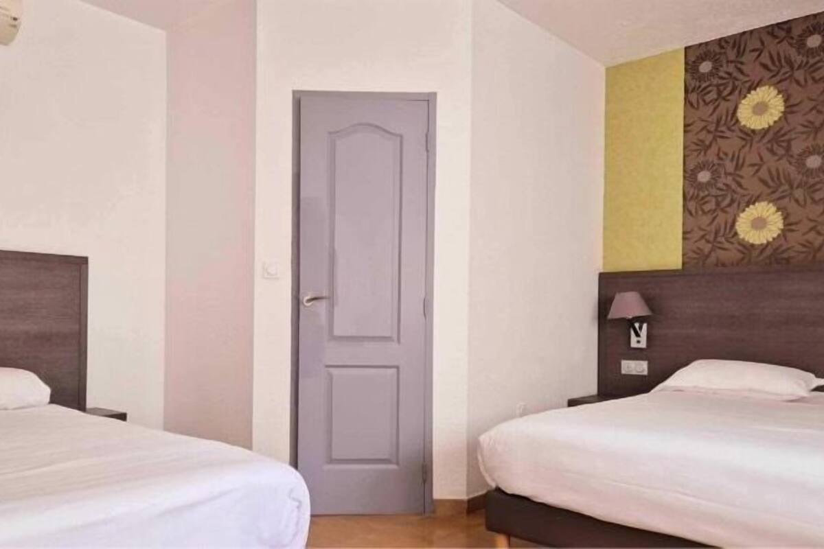 A hotel room with two beds, a grey door, and a wall with a sunflower pattern.