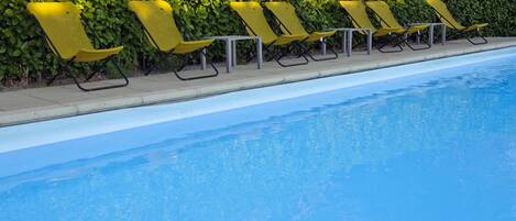 Un área junto a la piscina con una fila de sillas reclinables amarillas y un muro de setos al fondo.