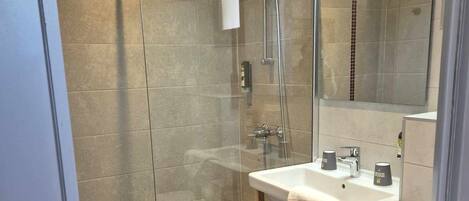 Un baño moderno con ducha envuelta en vidrio, tocador de madera y un espejo grande.
