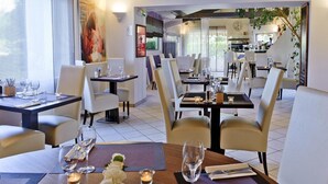 Un comedor moderno con mesas dispuestas para dos, con sillas blancas y una paleta de colores neutros.