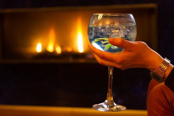 A hand holding a glass of water with a plant inside, in front of a fireplace with visible flames. - Els Caçadors (Ribes De Freser)