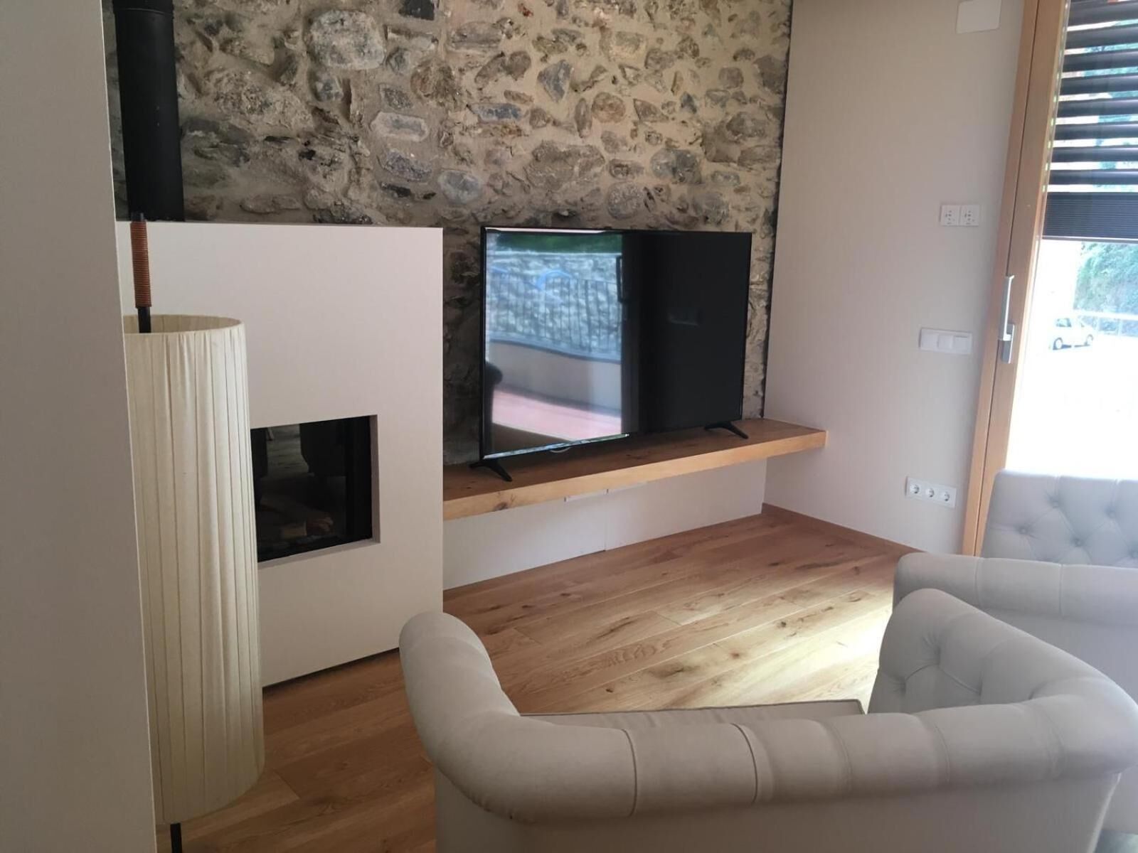A modern living room with a stone wall, a flat-screen TV on a wooden shelf, a white sofa, and a tall floor lamp.