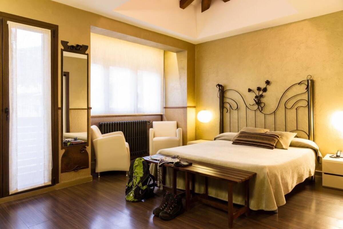 A hotel room with a bed, a chair, a table, a lamp, a mirror, and a radiator.