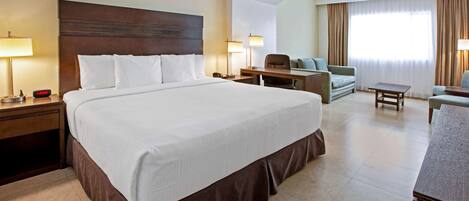 A hotel room with a large bed, a desk, a chair, and a sofa.