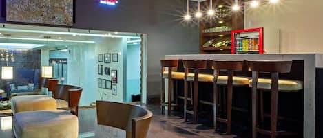 Zona de bar moderna con taburetes altos, una partición de vidrio y un letrero de neón.