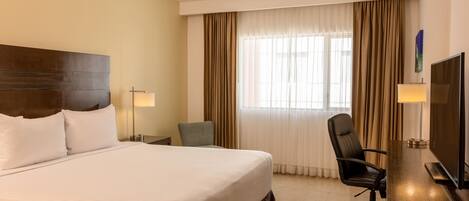 A hotel room with a large bed, a desk with a TV, a chair, and two lamps.