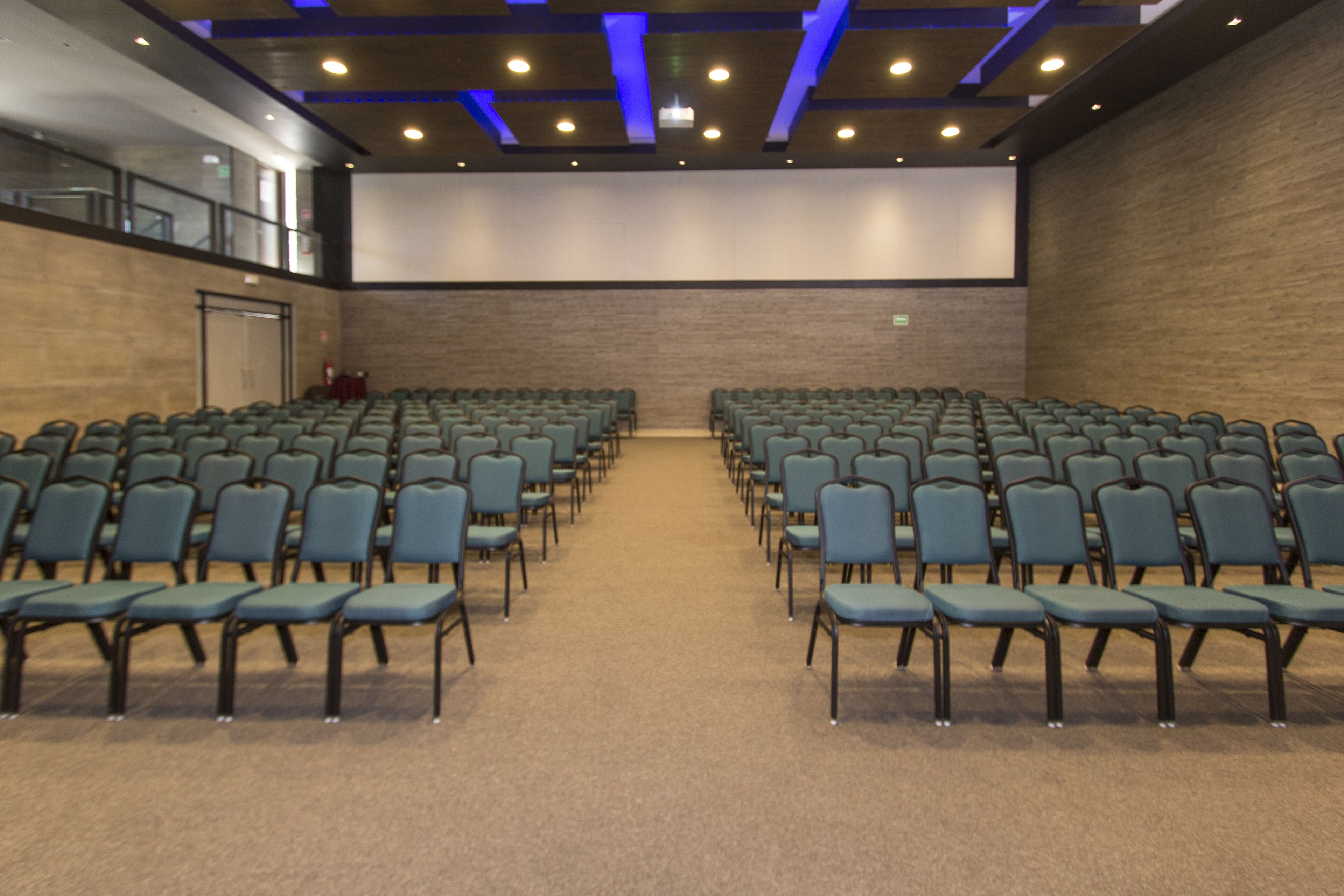 Konferenssitila, jossa on riveissä järjestettyjä tuoleja, suuri näyttö niiden edessä, matto lattialla ja puinen seinä.