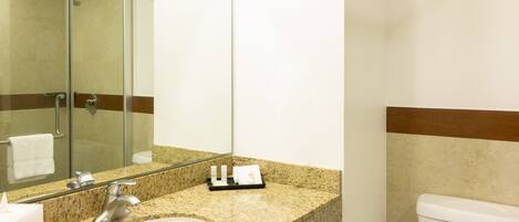 A bathroom with a granite countertop, a sink, a mirror, a glass shower enclosure, and a toilet.