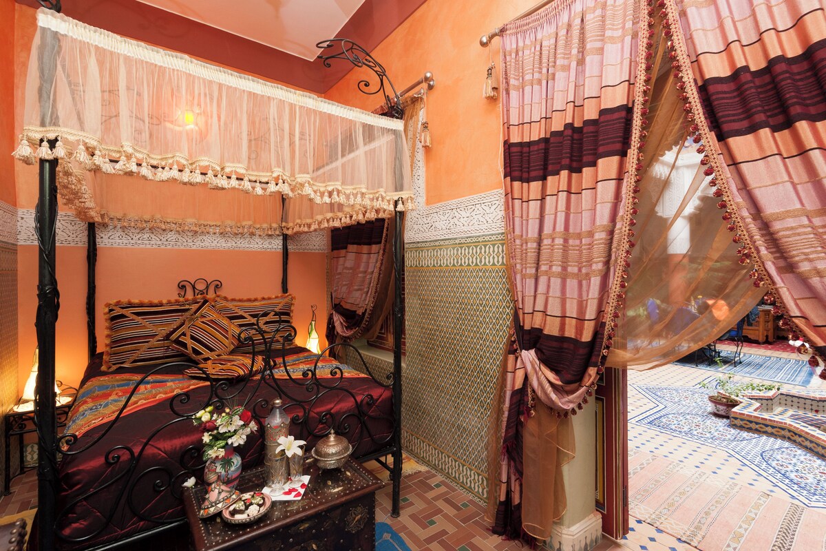 A traditional room with a four-poster bed, a decorative table with a vase of flowers, and a patterned floor.