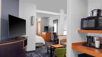 A hotel room with a flat-screen TV, a microwave, a coffee maker, a bed, a desk, and a chair.