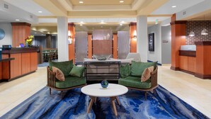 Eine Lobby mit einer Rezeption, einer Sitzecke mit zwei grünen Sofas, einem runden Tisch mit einer dekorativen Schale und einem gemusterten Teppich.