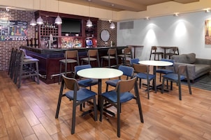 A bar area with a brick wall, multiple bar stools, and a round table with chairs. There is a sofa and a small table with chairs in the background.