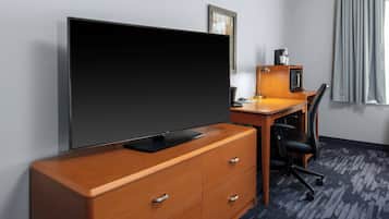 A hotel room with a large flat-screen TV, a wooden desk with a computer, a chair, and a microwave.