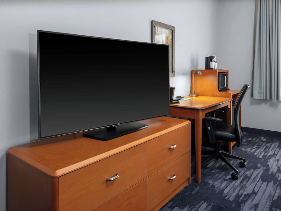 A hotel room with a large flat-screen TV, a wooden desk with a computer, a chair, and a microwave.