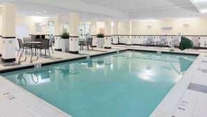 Ein großer, überdachter Swimmingpool mit klarem Wasser, umgeben von Liegestühlen und einer Sitzgruppe mit Tischen und Stühlen.