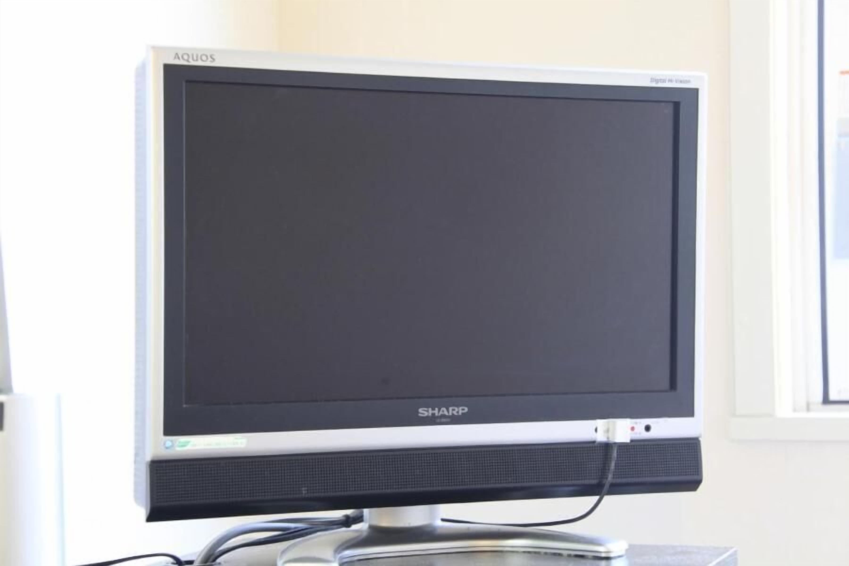 Un écran Sharp à fond noir, posé sur un bureau dont le plateau est en verre transparent.