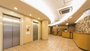 A hotel lobby with elevators, a reception desk, and a tiled floor.