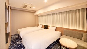 A hotel room with two beds, a sofa, a small round table, and a window with curtains.