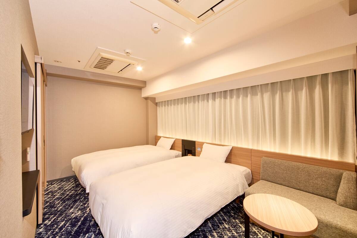 A hotel room with two beds, a sofa, a small round table, and a window with curtains.