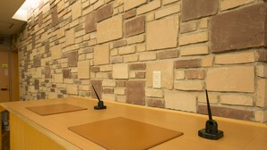 A reception desk with a stone wall background, a wooden counter, and two black telephone stands.